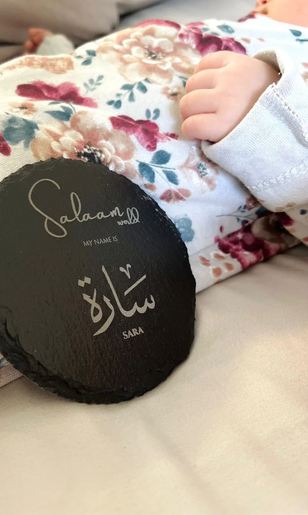 Round slate engraved “Salaam world, my name is Sara” in English and Arabic beside a newborn